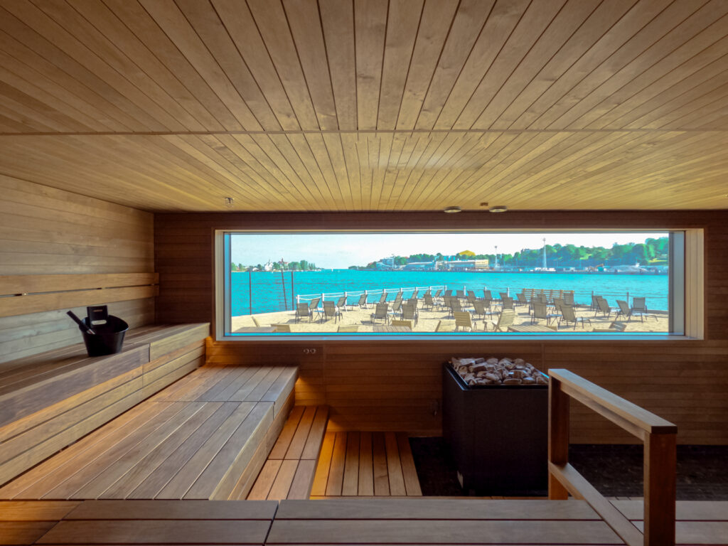 The inside of a sauna that includes a large window with a view to the sea.