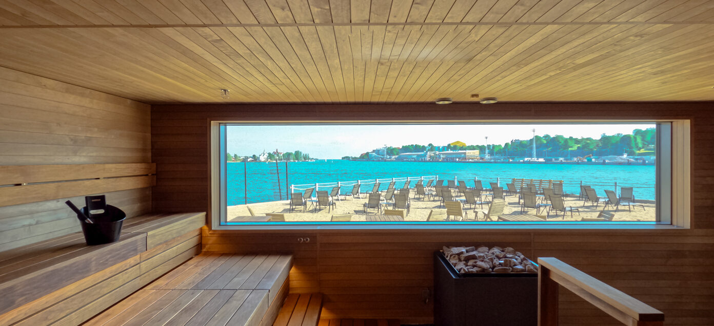 The inside of a sauna that includes a large window with a view to the sea.