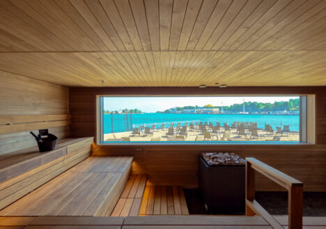 The inside of a sauna that includes a large window with a view to the sea.